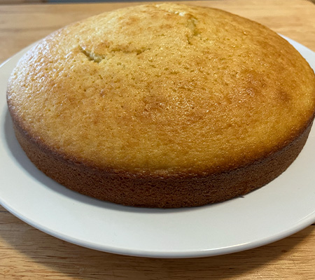 single layer olive oil cake on a white plate on wooden bench